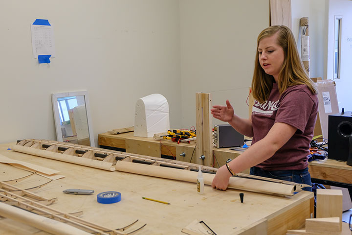 A student with a wooden airplane wing prototype on a construction table
