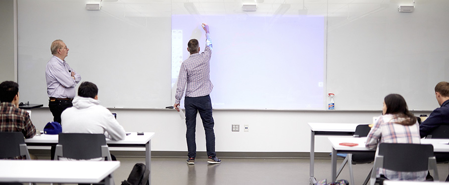 A professor beginning to write on a clean whiteboard in front of a class