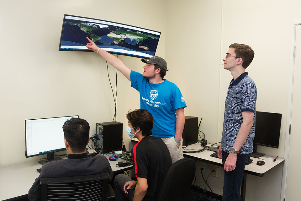 Group of students looking at a couple of different monitors for CubeSat project