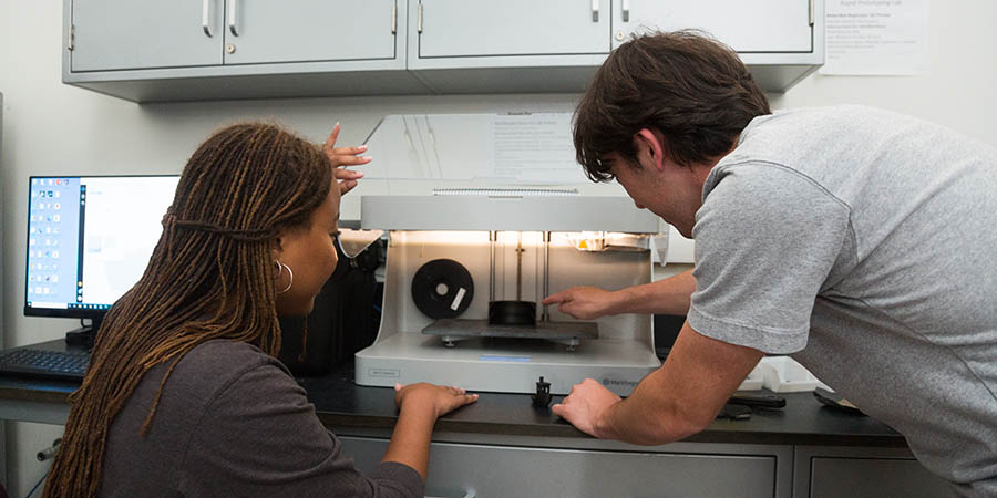 Female and male students working at 3D printer