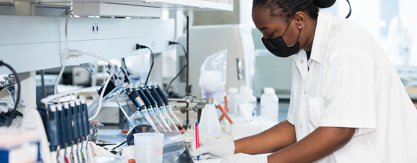 A student in a lab taking notes while wearing gloves and mask